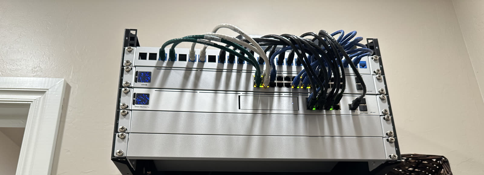 Wall-mounted rack with a labeled patch panel and color-coded patch cords to a switch